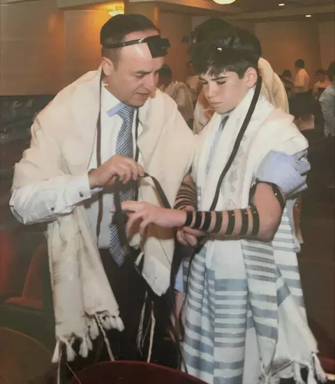 David Mizrahi's father instructing him how to don phylacteries (Tefillin) for the first time at his Bar Mitzvah.