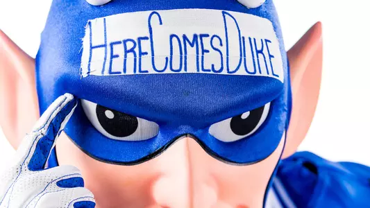 Blue Devil mascot points to text on his suit, "Here comes Duke."