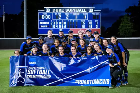 The Duke softball team poses in front of the scoreboard after winning the 2022 Durham Regional
