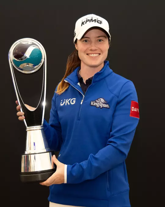 LeLeona Maguire posing with a trophy, wearing a blue sports jacket and white cap.ona Maguire posing with a trophy, wearing a blue sports jacket and white cap.