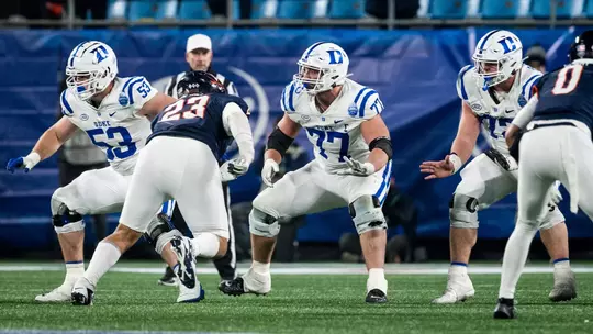 Duke's offensive line, all wearing a white helmet, white jersey and white pants, move in sync following the snap versus No. 16 Virginia in the 2025 ACC Championship Game.