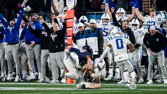 Duke linebacker Luke Mergott, wearing a white helmet, white jersey and white pants, lays on the field with the ball in his arms following his game-winning interception versus No. 16 Virginia in the 2025 ACC Championship Game.