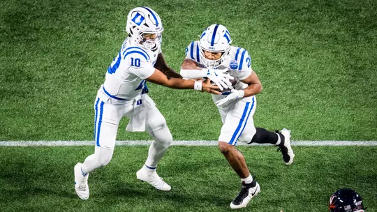 Duke quarterback Darian Mensah, wearing a white helmet, white jersey and white pants, hands the ball off to running back Nate Sheppard, wearing the same uniform, during the ACC Championship Game versus No. 16 Virginia.