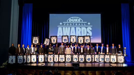 Members of the 2025 Duke football senior class hold their framed jerseys above their heads to cap the program's annual awards banquet.