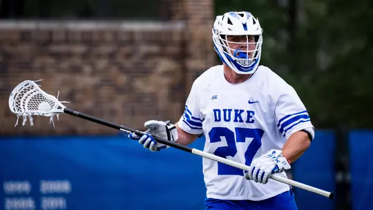 Charlie Johnson stands in his white jersey with his lacrosse stick during a Duke men's lacrosse game.