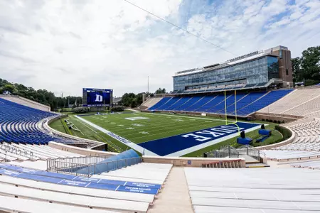 Side view of Brooks Field at Wallace Wade Stadium, highlighting the end zone, the expansive blue seating area, and the large scoreboard under a partly cloudy sky.