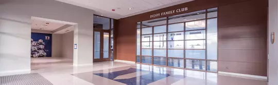 Entrance to the DeJoy Family Club featuring large glass doors and frosted floor-to-ceiling windows framed by dark wood paneling.
