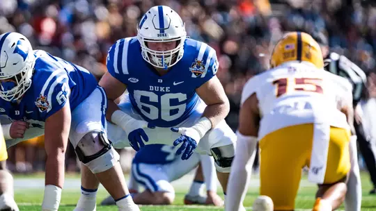 Duke offensive lineman Caleb Dorris, wearing a white helmet, blue jersey and white pants, leans over and waits for a snap during the 2025 Tony the Tiger Sun Bowl, which Duke won 42-39 against Arizona State inside Sun Bowl Stadium.