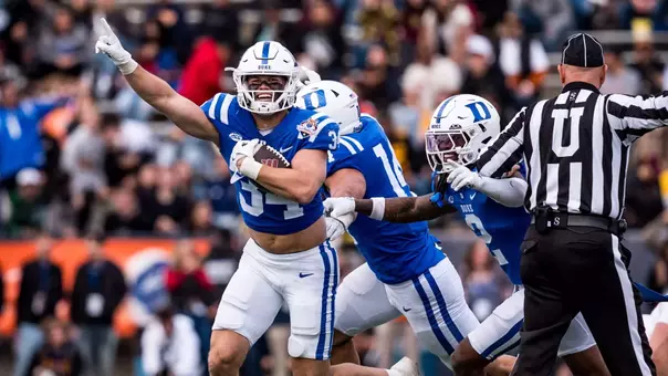 Duke linebacker Luke Mergott, wearing a white helmet, blue jersey and white pants, smiles, holds his index finger in the air, cradles the football in his arm and celebrates the game-sealing interception to lift Duke to a 42-39 victory against Arizona State in the 2025 Tony the Tiger Sun Bowl inside Sun Bowl Stadium.