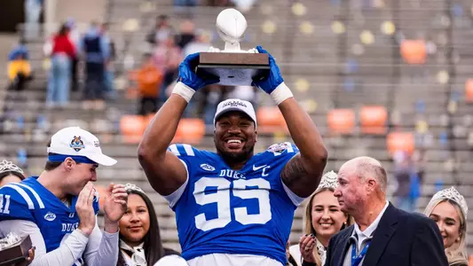 Duke defensive tackle Aaron Hall, wearing a white hat and blue jersey, lifts his Jimmy Rogers Jr. Most Valuable Lineman trophy above his head following Duke's 42-39 victory against Arizona State in the 2025 Tony the Tiger Sun Bowl.