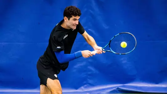 Duke men's tennis' Gerard Planelles Ripoll, wearing a black shirt and black shorts, take a backhand swing during a match.