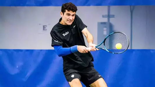 Duke men's tennis' Gerard Planelles Ripoll, wearing a black shirt and black shorts, takes a backhand swing during a match.
