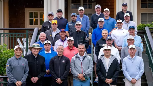 The participants of the 19th annual Southern Company Peach Bowl Challenge charity golf tournament stand on stairs outside and pose for a photo.