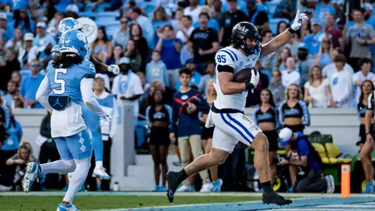 Duke tight end Jeremiah Hasley, wearing a black helmet, white jersey and white pants, celebrates a touchdown with one arm raised during the Blue Devils' 32-25 victory at North Carolina on November 22, 2025.
