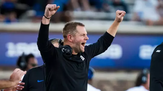 Duke defensive coordinator Jonathan Patke, wearing a black shirt, holds his arms up in celebration during Duke's 62-7 victory against William & Mary.