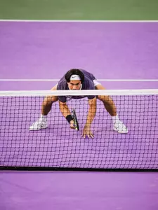 Duncan Chan in his purple shirt on TCU purple courts and down low at the net, eagerly waiting to volley