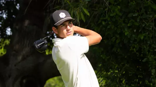Sam Udovich swings a golf club and stares into the sun with a follow through