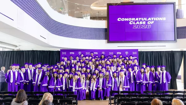 TCU athletics Class of 2026 posing for a photo in their graduation gowns with Athletic Director Mike Buddie