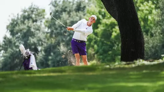 Nathan Miller swings a club under a tree wearing purple shorts and a white shirt