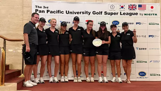 The TCU women's golf team poses together on stage with an engraved silver plate after finishing in second place at the Pan Pacific University Golf Super League tournament.