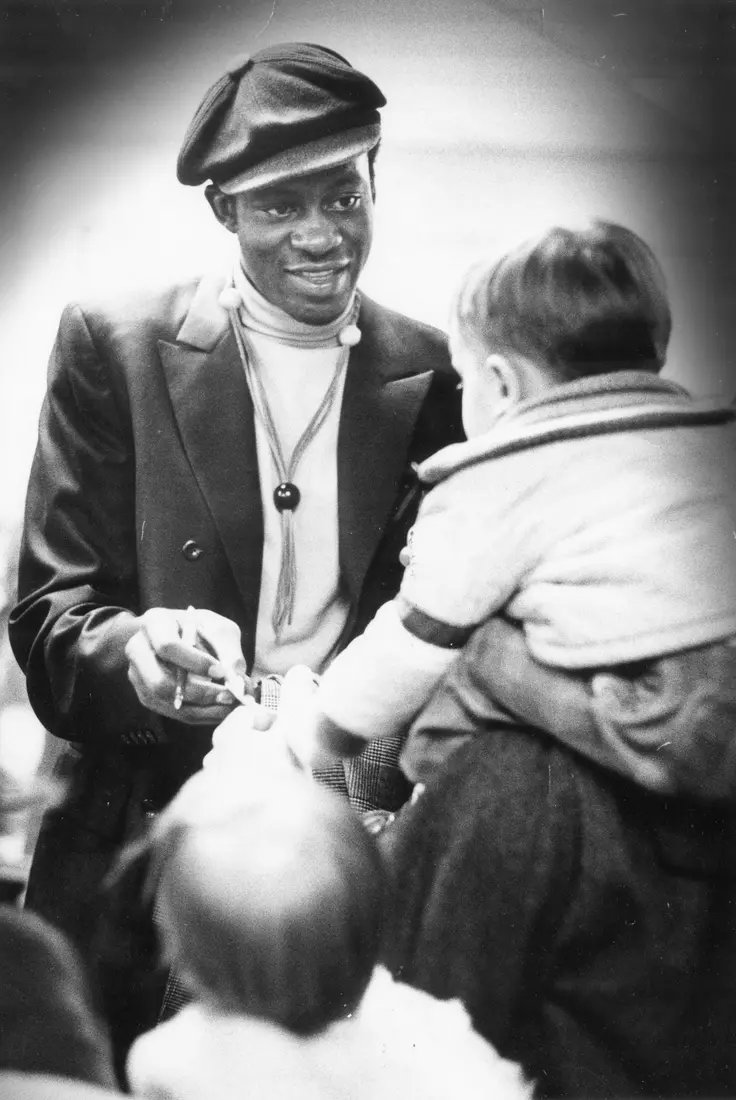 Marquette basketball player Jim Chones, dressed in casual clothing, speaks to a child at a gathering, 1972-1973.
