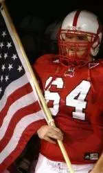 An NC State scout team member carries the American flag onto the field at every home game.