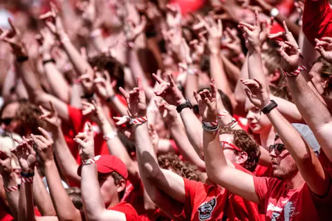Fans hold up wuf hands during football game in Carter-Finley Stadium.