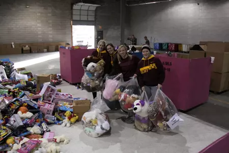 Gophers pose before tossing bears into the pile of toys.