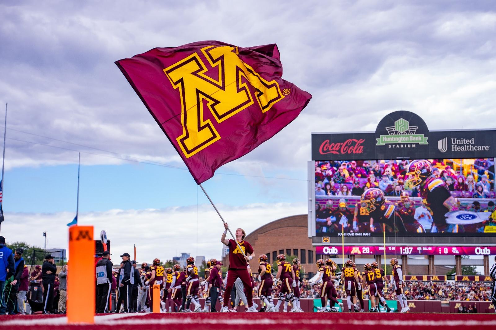 A cheerleader waves a M branded flag at a football game in 2025.