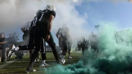 Cal Poly players pass through the tunnel and fog prior to a 2021 game.