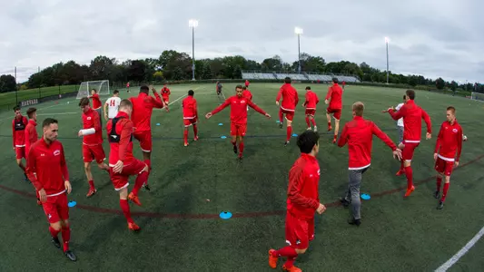 Members of the men's soccer team warm up before the Harvard game by doing running drills around tiny cones.