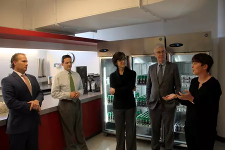 Several BU dignitaries are in a discussion in front of the fridges containing drinks inside the Terrier Fueling Station.