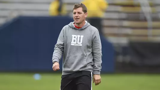 Associate Head Coach Scott Black is wearing sweatshirt and shorts. He's walking across the field.