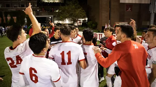 The BU men's soccer team gathers around in a standing huddle to celebrate a 2-1 overtime victory over Colgate