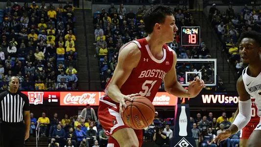 Side angle view of Max Mahoney dribbling near the sideline with a West Virginia defender in front of him.