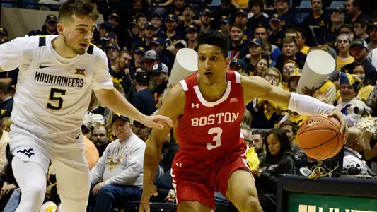 Alex Vilarino has the ball in his left hand as he dribbles with a West Virginia defender to his right side.