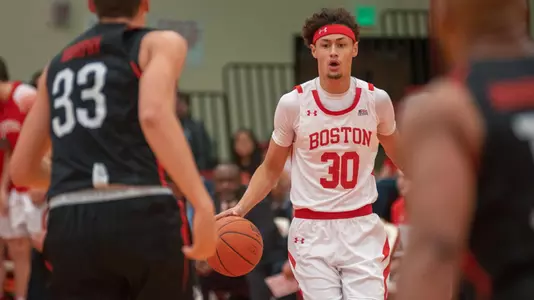 Javante McCoy is bringing the ball up the court from an angle with a defender to his right and left.