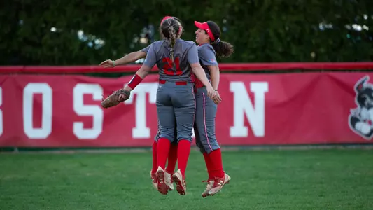 Three BU softball outfielders do a combined flying chest bump.