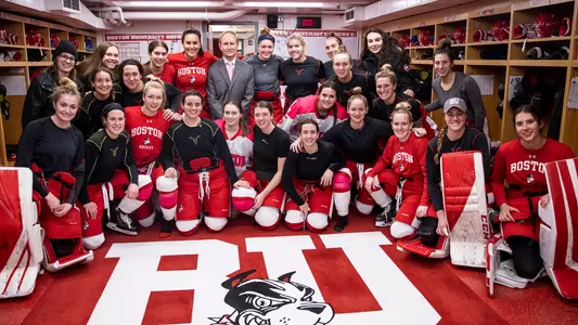 Brian Durocher and the Boston University women's ice hockey team pose for a picture in the locker room after Durocher's 300th win