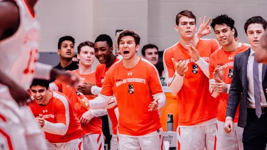Members of the Boston University men's basketball bench jump up in celebration following a play.