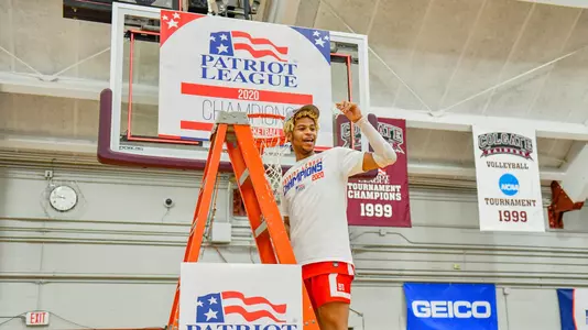 Ethan Brittain-Watts waves to the crowd while standing on the ladder under a hoop at the 2020 Patriot League men's basketball championship postgame celebration.