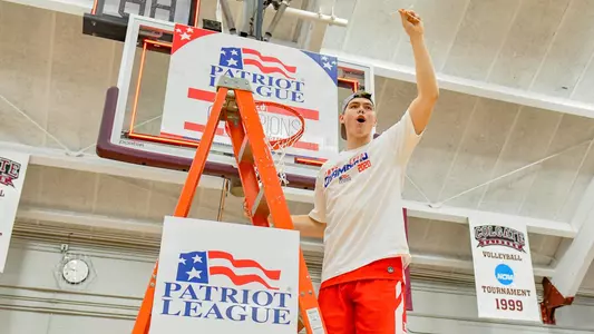 Jack Hemphill waves to the crowd while standing on the ladder under a hoop at the 2020 Patriot League men's basketball championship postgame celebration.