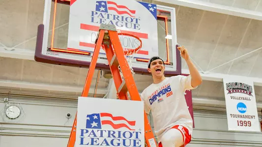Tarkan Taboglu waves to the crowd while standing on the ladder under a hoop at the 2020 Patriot League men's basketball championship postgame celebration.