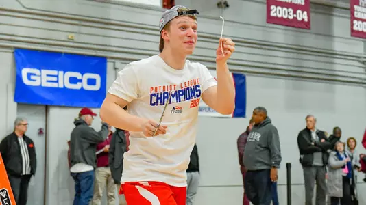 Michael Quinn holds a piece of string he cut off from the net after standing on the ladder under a hoop at the 2020 Patriot League men's basketball championship postgame celebration.