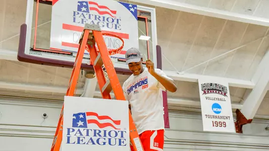 Tim Uzoegbu signals to the crowd with a string in hand while stepping down the ladder under a hoop at the 2020 Patriot League men's basketball championship postgame celebration.