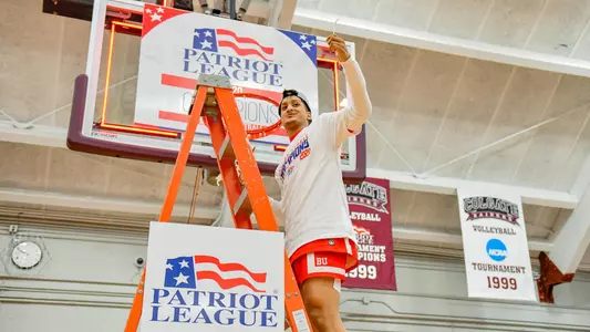 Alex Vilarino waves to the crowd while standing on the ladder under a hoop at the 2020 Patriot League men's basketball championship postgame celebration.