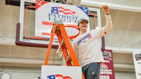 Garrett Pascoe waves to the crowd while standing on the ladder under a hoop at the 2020 Patriot League men's basketball championship postgame celebration.