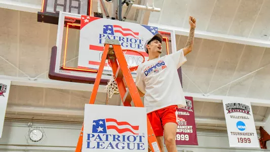 Javante McCoy waves to the crowd while standing on the ladder under a hoop at the 2020 Patriot League men's basketball championship postgame celebration.