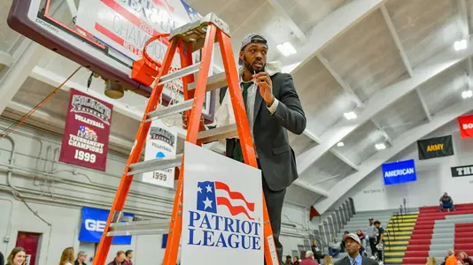 Director of Operations Al Paul looks to the crowd while standing on the ladder under a hoop at the 2020 Patriot League men's basketball championship postgame celebration.