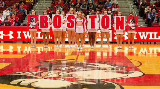 The BU cheerleading squad holds up individual signs spelling out Boston at midcourt during a basketball game.